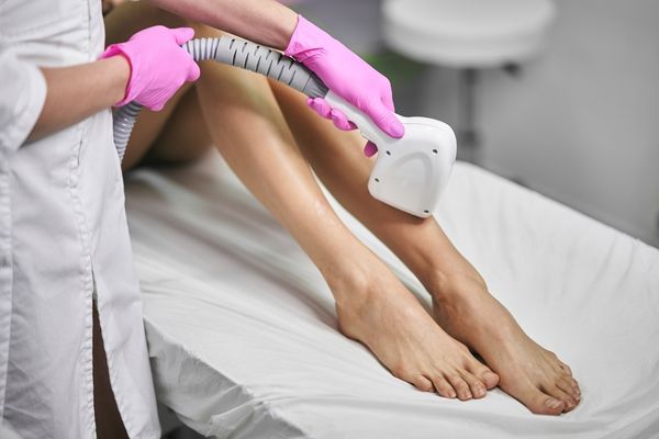 A woman receiving laser hair removal treatment on her leg from a professional technician