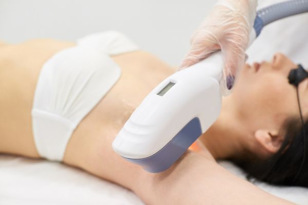 A beautiful woman with black safety goggles on her eyes receiving laser hair removal treatment on her underarm from a professional technician