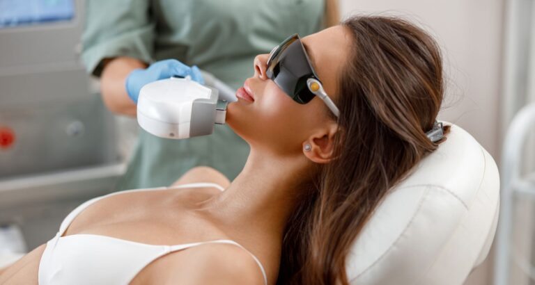 A young woman receiving laser rejuvenation treatment on her chin from a professional technician while wearing safety goggles