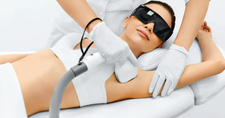 A woman lying on a bed with goggles on her eyes and a technician applying an IPL laser device to her underarm